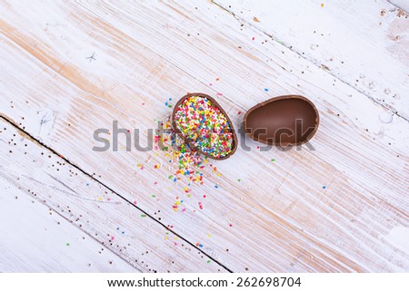 Chocolate egg filled with colorful candy sprinkles on white wooden surface. High angle view of beautiful sweet cocoa egg broken in two. Horizontal, copy space, no retouch.