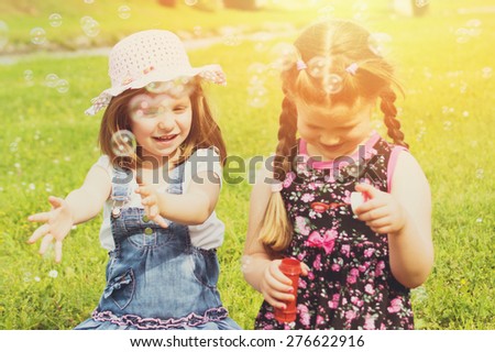 Two cute little girls on picnic in park on sunny summer day. Little sisters playing with water balloons outdoors in nature. Horizontal, retouched, filter, vibrant colors.
