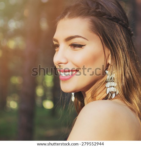 Closeup portrait of beautiful smiling bohemian young woman with silver butterfly boho earrings with balayage dyed hair and braid outdoors in park in summer. Square format, retouched.
