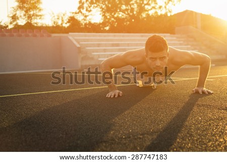 Handsome fit shirtless Caucasian young man doing push-ups outdoors on sunny summer day. Guy workout in urban environment on sunset. Natural light, mild retouch, no filter, horizontal.
