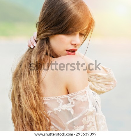 Closeup head shot of gorgeous young blonde woman at the beach. Beautiful girl with long hair looking down wearing makeup and sheer beige dress. Square format, retouched, vibrant colors.