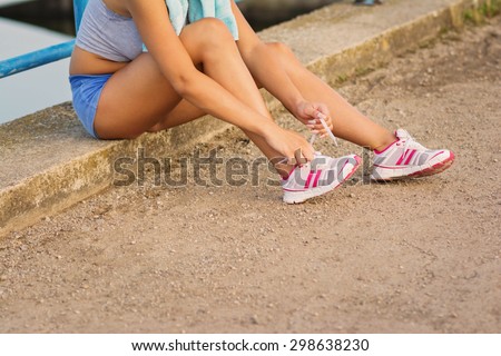 Closeup of unrecognizable fit young woman tying shoelaces after running wearing blue shorts and tank top sitting. Horizontal, mild retouch, to filter.