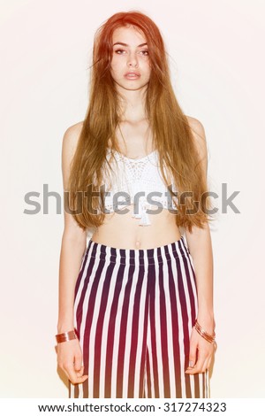 Fashionable young woman with long messy hair in summer outfit. Teenage girl with messy bun wearing white crochet crop top and striped pants posing. Pastel filter applied, medium retouch, vertical