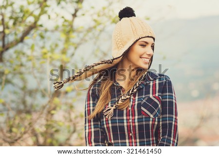 Beautiful modern urban young woman wearing blue and red plaid shirt and knitted beige and black hat. Trendy teenage girl in autumn outdoors. Horizontal, medium retouch, matte filter.
