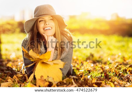 Happy young woman in park on sunny autumn day. Cheerful beautiful girl in gray sweater and floppy hat outdoors on beautiful fall day. Retouched, vibrant colors, back lit, natural light.