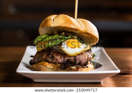 Delicious burger with onion, fried eggs, asparagus and french fries.