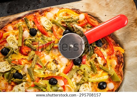 Top view of a vegetables pizza and its cutter.