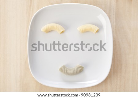 Funny pasta face with italian raw handmade pasta on a white dish.