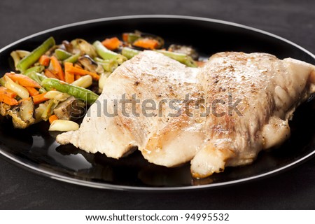 Delicious cooked pork meat, ready to eat with vegetables on a black dish.