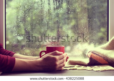 red mug of hot drink, when behind a window is rain / cozy home atmosphere