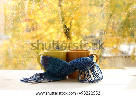 mugs tied together warming scarf on the background of a wet window after the rain / warm drinks for the autumn mood