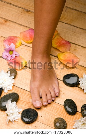 bronzed foot on sauna board floor with stones, rose-petals and flowers