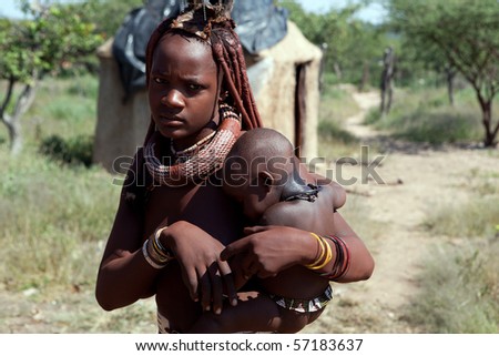 KAOKOLAND, NAMIBIA - MAY 9: Unidentified Himba women with red clay hair, traditional decorations and her baby in front of traditional cabin on May 9 2010, in Himba Village near the Kamanjab Namibia