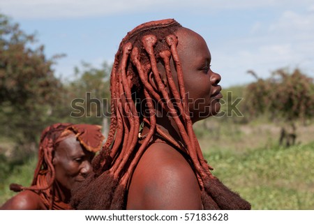 KAOKOLAND, NAMIBIA - MAY 9: Unidentified Himba women with red clay hair  wait for folk art products trade to begin on May 9 2010, in Himba Village near the Kamanjab Namibia