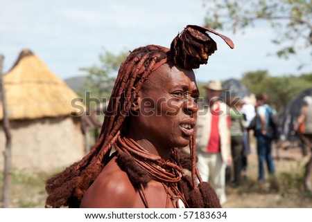 KAOKOLAND, NAMIBIA - MAY 9: An unidentified Himba woman with red clay hair watches Geman tourists arrive on May 9 2010, in Himba Village near the Kamanjab Namibia