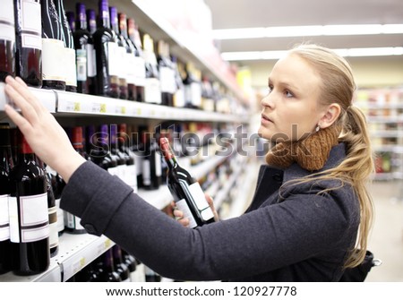 Young Woman Is Choosing Wine In The Supermarket.