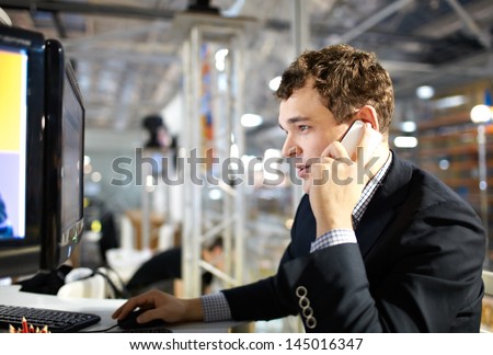 The young man works at a computer and talking on the phone.