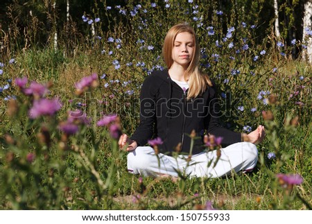 Lotus yoga pose. Woman meditating in the city park at summer morning. Beautiful blue flowers in foreground.