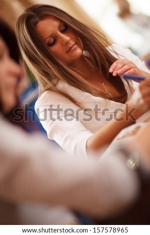Serious beautiful young businesswoman in a meeting writing notes, tilted view past the shoulder of a female colleague