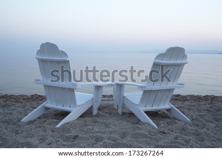 Empty white painted wooden deck chairs on a beach overlooking a calm ocean