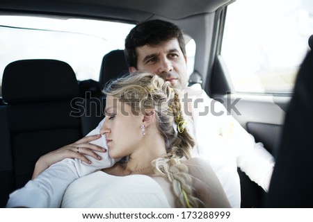 Beautiful tired young blond bride sleeping on her husbands shoulder in the back seat of a motor vehicle