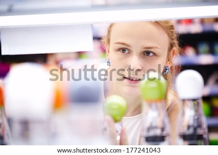 Young blond woman carefully analyzing products in a store - view through products