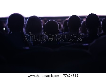 Middle shot of sihouettes of people from back watching cinema or performance with white empty space