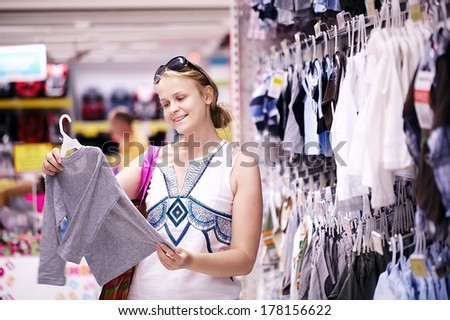 Attractive young mother shopping for childrens clothes in a retail clothing store viewing items on a rack