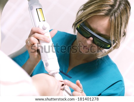 Young female beautician or nurse in a skin clinic doing laser skin treatment on a woman to rejuvenate her skin or treat scar tissue