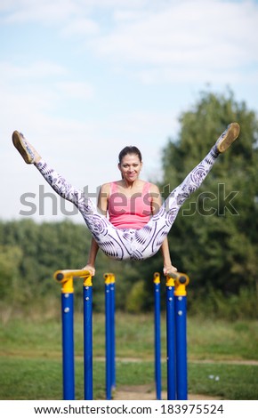 Athletic attractive young female gymnast exercising on parallel bars balancing on her hands with both her legs raised high in the air