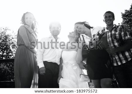 Low angle view of a happy smiling newlywed bride and groom posing against the sun with their friends, monochrome image with sun flare