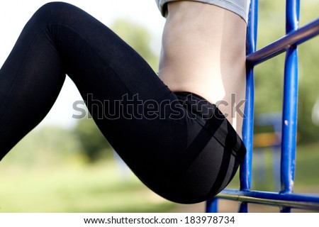 Close up of the fit toned female body and tight flat stomach of a young woman athlete hanging from a metal frame outdoors