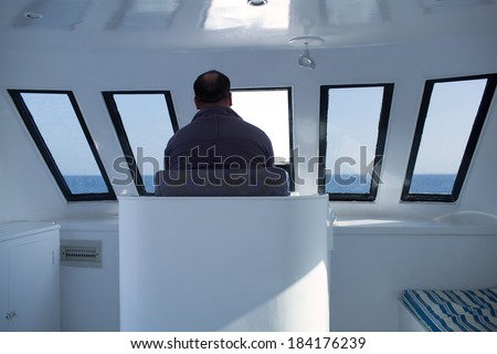 Man navigating a boat sitting in the captains chair during a cruise overlooking the ocean ahead, view from behind
