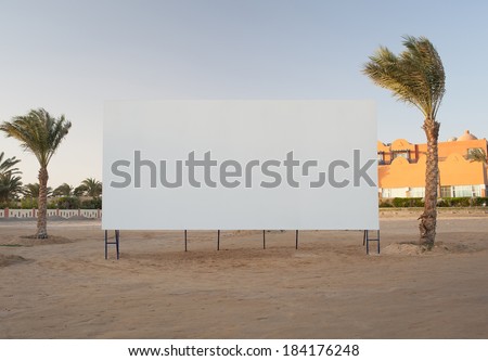 Blank white billboard with copyspace for your advertisement or movie flanked by two palm trees