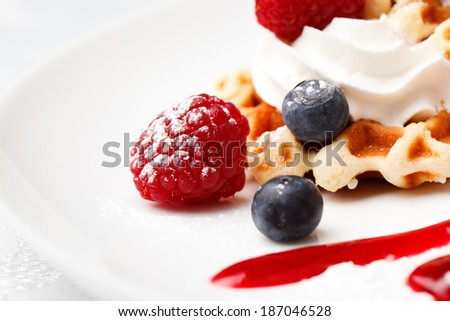 Golden waffle served with a dollop of whipped fresh cream and raspberries and blueberries drizzled with syrup or berry coulis