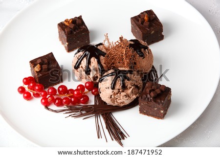 Scoops of creamy chocolate ice cream served with chocolate bonbons and a bunch of fresh red currants garnished with chocolate strands for a gourmet dessert