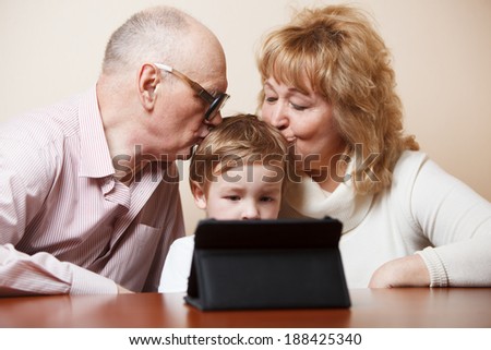Grandparents kissing their little grandson who is busy with touchpad