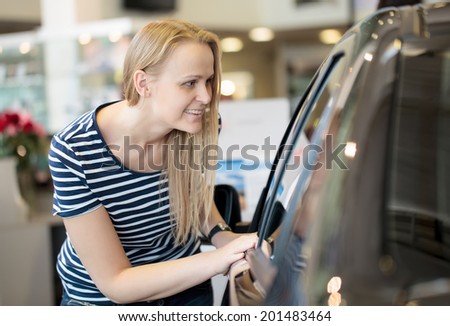 Woman admiring a car at an auto show or in a car shop showroom bending down to peer through the window with a keen expression