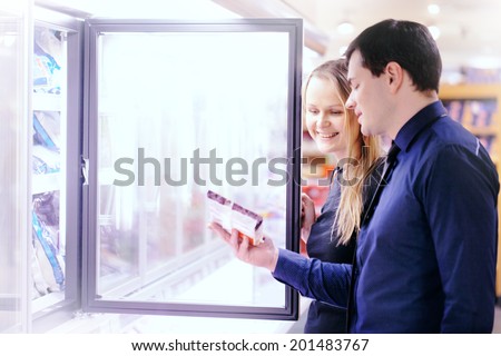 Couple in the frozen goods section of a grocery store picking out food from the freezer