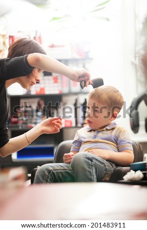 Little boy having a hair cut in a salon sitting in the chair as the hairdresser combs and cuts his hair, low angle distance view