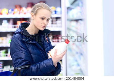 Woman in grocery holding a bottle of milk reading the label intently