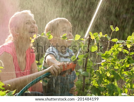 Laughing young mother and her small son playing with a jet of water from a sprinkler nozzle allowing the spray to fall back over themselves in a summer garden