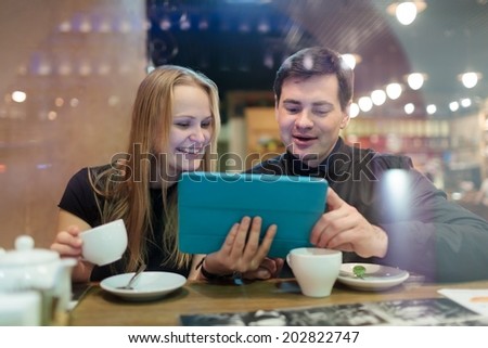 Young people drinking coffee in cafe and looking on pad