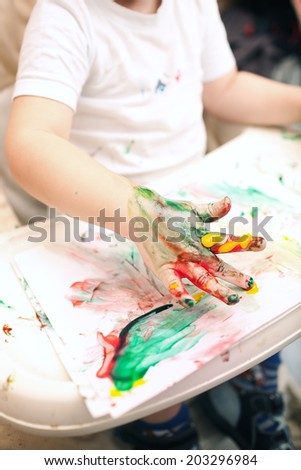 Little boy painting with colorful finger-paints. Colored hand and abstract painting in focus