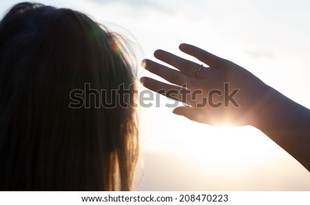Back close-up shot of a woman looking in the distance hiding from the sun with a hand
