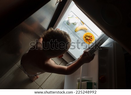Little hungry boy at night searching something tasty in open fridge