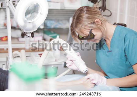 Female cosmetician in safety glasses at work. She providing a foot treatment with a laser