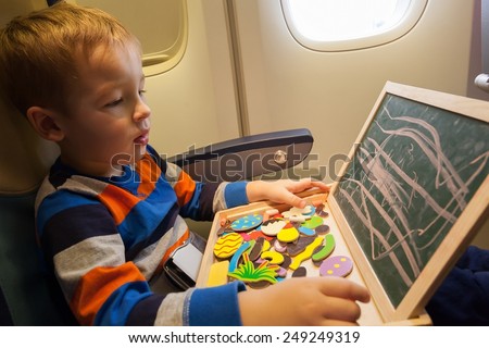 Little boy in the plane drawing on small board with chalk. Entertainment during flight
