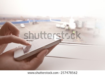 Woman using smart phone by the window at aiport
