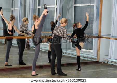 Choreographer helping young ballet dancer to have right position. Exercising at the barre by the mirror
